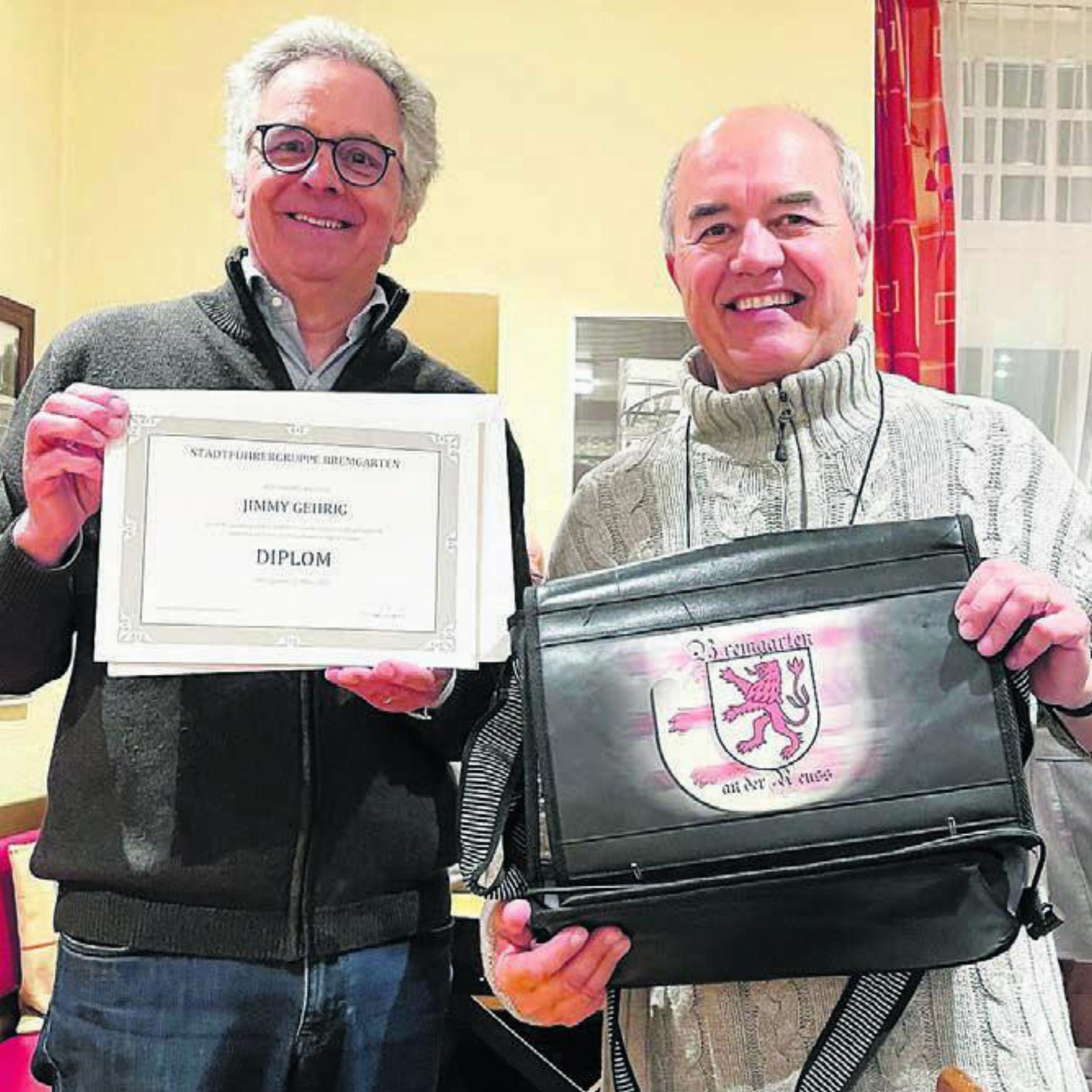 Jimmy Gehrig (rechts) wird vom Vorsteher der Stadtführergruppe Bremgarten, Reto Jäger, als neues Mitglied aufgenommen. Der «Jasskönig» bekommt nun auch die Insignien der Stadtführer: Nach Krone und Zepter sind dies die Tasche mit Stadtwappen und das Diplom.